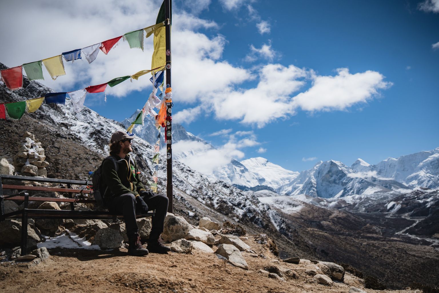 Max Roper on a bench beneath Tibetan prayer flags, looking out over the Himalaya in the Khumbu